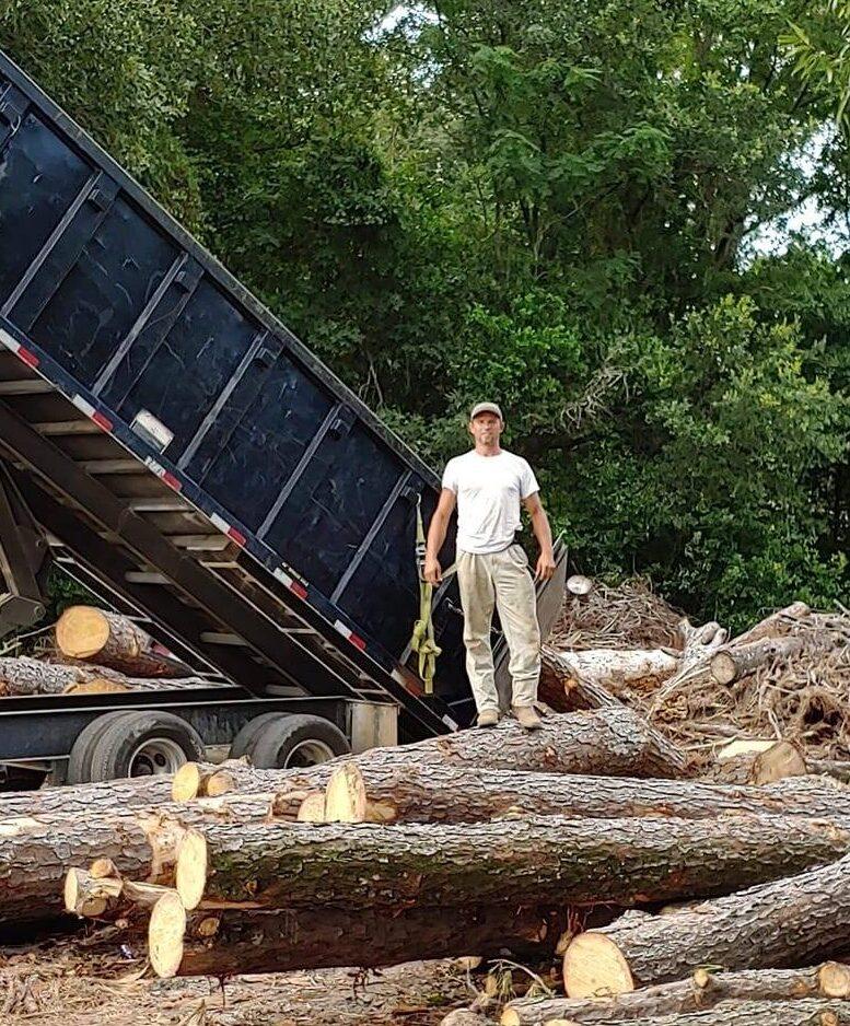 Ferrell Morgan standing on cut logs with dump bed behind him.